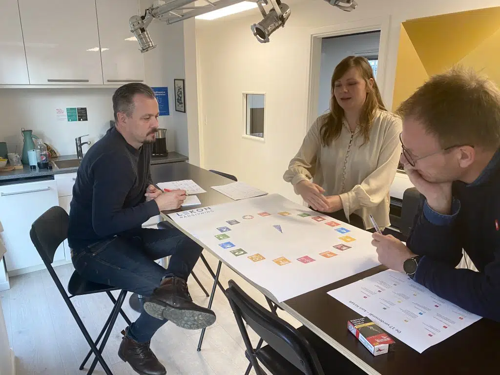 Tre medarbejdere diskuterer verdensmålene ved et bord